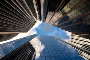 An upward perspective capturing glass skyscrapers reflecting the dynamic sky, embodying an urban environment's vibrancy and the essence of modern city life in London UK
