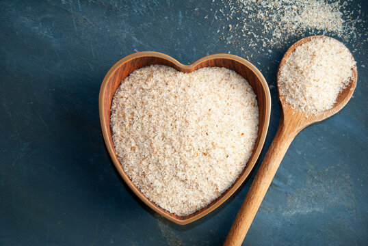 Whole psyllium husks in a rustic wooden heart-shaped bowl with a spoon.