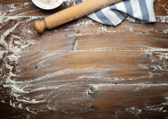 Wooden pastry board with scattered flour, rolling pin and dishcloth, top view, space for text.