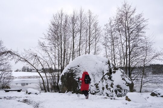 Huge Devil Stone by Kamienne Lake and silhouette of woman in red coat in winter scenery. Zurawie Blota (Mud Cranes)  Nature Reserve, Kashubian Landscape Park, Mirachowskie Forests, Pomerania, Poland.