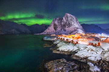 Aurora borealis northern lights over Lofoten Islands, Reine, Hamnoy, Norway, sea rocky shore and fishing villages red rorbu houses © ValentinValkov