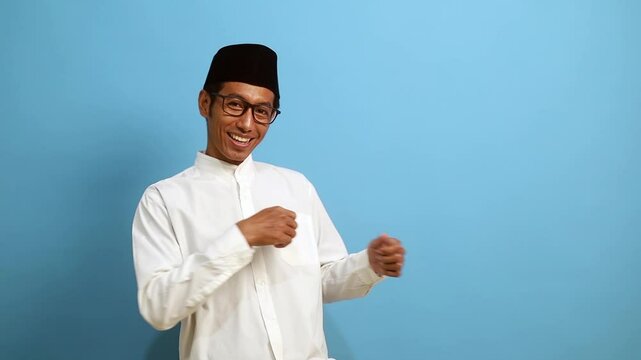 Happy asian muslim man standing while pointing sideways on empty space and showing thumbs up