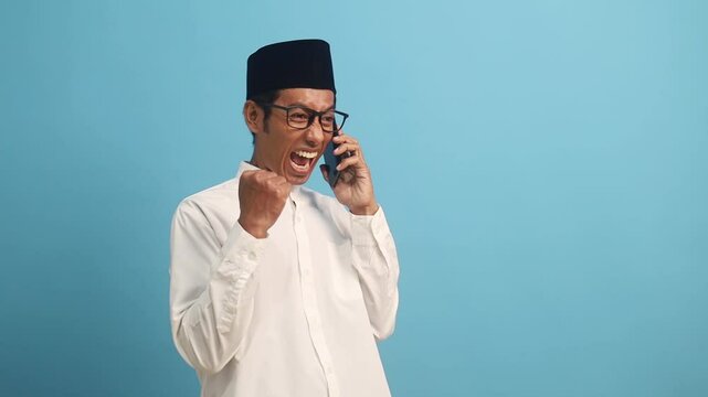 Surprised asian muslim man celebrating his success while getting good news from his phone