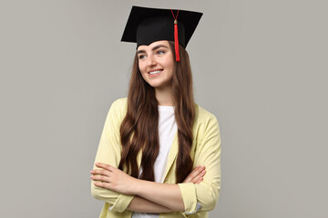 Happy student with crossed arms after graduation on grey background