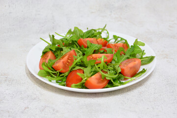 a plate of tomatoes with arugula on the gray background 