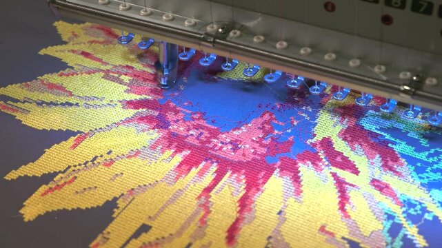 A sewing machine is in use, stitching colorful flower of fabric. The machine is bright and shiny, and the fabric