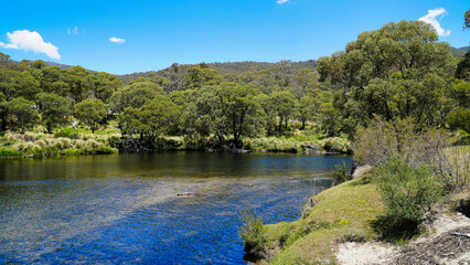 Jindabyne, New South Wales Australia.Serene river view with lush greenery under a clear blue sky at midday in a tranquil natural setting