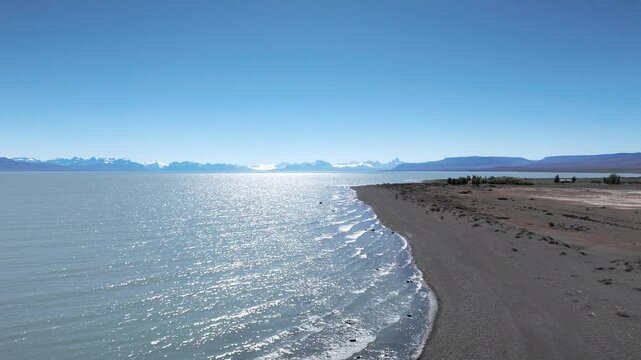 Whispers of the Waves. Experience the breathtaking beauty of Argentina's coastline! This drone footage captures stunning waves rolling onto a sandy beach with majestic mountains in the background.