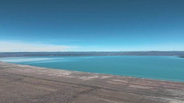 Mountain Lake. Discover a hidden paradise nestled in the heart of Argentina. This drone footage reveals a tranquil lake mirroring the majestic mountains, its shores fringed by pristine, golden sand. 