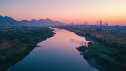 Serene River Flowing Towards Industrial City at Dawn with Majestic Mountains in Background.