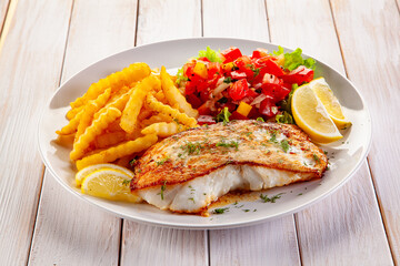 Fish dish - fried cod fillet with fresh salad and french fries served on wooden table