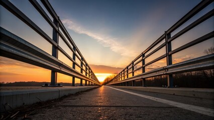 Obraz premium A lole shot emphasizes the height and strength of the guardrails framing them against the sky at dusk. The setting sun casts a warm glow over the metal creating a striking