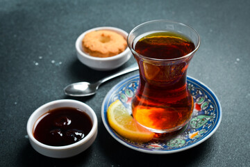 Traditional Turkish serving of aromatic tea in a glass. On a black stone background.