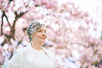 Spring close up portrait of beautiful 55 - 60 year old woman posing with magnolia tree