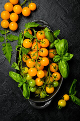 Cherry tomatoes. Ripe fresh yellow orange tomatoes with green tails, leaves on a black stone background flat lay top view. Vegetables, healthy vegan organic food