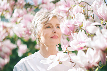Spring close up portrait of beautiful 55 - 60 year old woman posing with magnolia tree