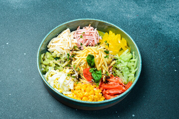 A plate of colorful vegetable salad made of cucumber, paprika, tomatoes, potatoes and boiled sausage. On a dark stone background.