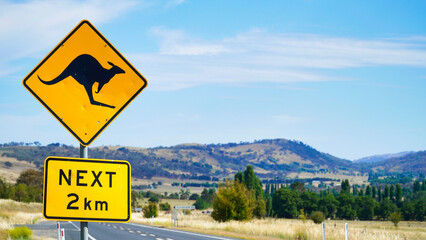 Kangaroo crossing sign near rural road in Australia with scenic landscape in the background