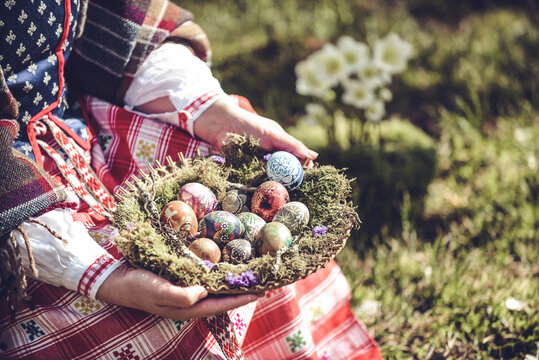 Woman in traditional Lithuanian clothes holding basket filled with Easter eggs
