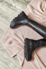 Trendy model poses with stylish black boots on a cozy pink sweater in a modern setting