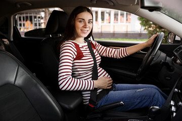 Smiling pregnant woman with safety belt driving car