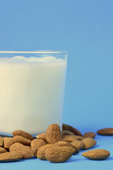 Vertical shot. Natural almonds and milk in a glass, on a blue background, copy space.