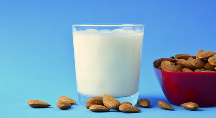 Almond milk, scattered natural almonds and milk in a glass, on a blue background.