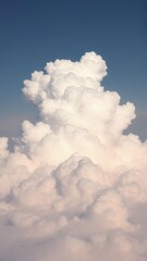 A towering cumulus cloud rises against a clear blue sky, with billowy white formations creating a textured,