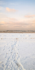 Tranquil winter beach with snowy shoreline and serene ocean waves at sunrise