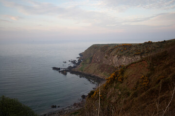 Naklejka premium Scenic coastal view in Stonehaven, Scotland showcases cliffs meeting the quiet sea at dusk