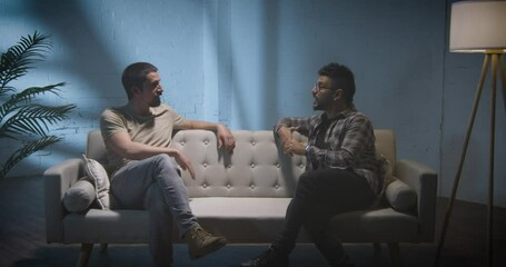 Two men on a couch interview scene, talking and sharing stories, podcast concept.