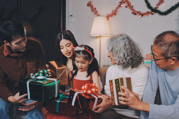 Portrait of Asian family exchanging presents during christmas at home. Attractive happy people holding gift box, celebrate holiday thanksgiving, xmas eve tradition in living room in house together.