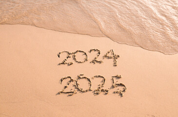 Handwritten inscription 2024 and 2025 on the beach in the sunset time. The concept of Goodbye 2024 and Happy New Year 2025