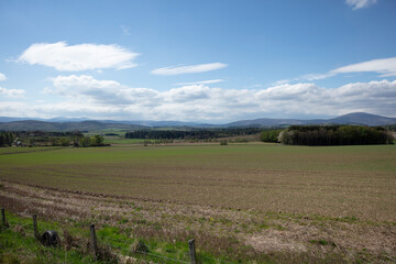 Expansive Scottish countryside view features rolling hills under a blue sky dotted with clouds