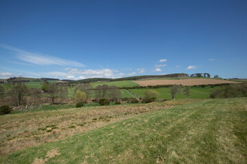 Explore the ancient earthworks in Scotland under a bright blue sky and scattered clouds during a tranquil afternoon