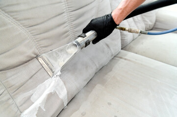 Cleaning concept. Man cleans sofa in the room. Virus prevention sanitizing inside. Process of deep furniture cleaning. Professionally chemical cleaning