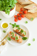 Bruschetta toasts with mozzarella, cherry tomato and basil leaves on white wooden table