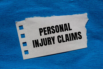 Personal injury claims message written on ripped torn paper piece with blue background. Conceptual...
