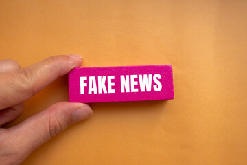 Fake news message written on pink wooden block with orange background. Conceptual fake news symbol....