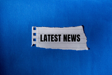 Latest news message written on ripped torn paper piece with blue background. Conceptual latest news...