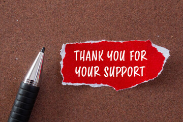 Thank you for your support message written on ripped torn red paper piece and a pen with brown...