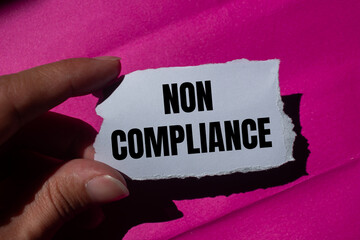 Non compliance message written on ripped torn paper piece with a pink background. Conceptual non...