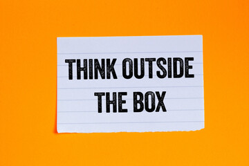 Think outside the box message written on ripped torn white paper piece on orange background. Conceptual think outside the box symbol. Copy space.