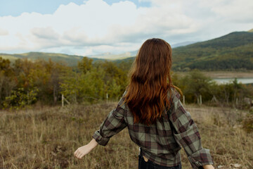 Woman with vibrant red hair standing in picturesque field with majestic mountains in background,...