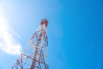 A towering red-and-white communication tower against a bright blue sky, symbolizing connectivity...