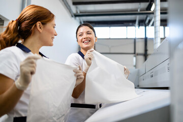 Dry cleaning workers preparing clean pillow cases for ironing in industrial laundry machine.