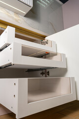 A modern, empty kitchen cabinet featuring sleek white design and transparent storage spaces.