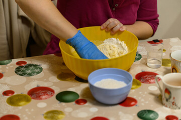 A female hand with a blue glove is mixing the dough.
