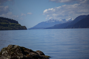 Scenic view of a tranquil Scottish lake surrounded by mountains on a clear day with a vibrant blue sky