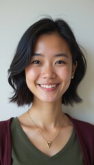 A joyful young woman with shoulder-length dark hair beams with a warm smile, showcasing her friendly personality. Her casual outfit and delicate necklace add a touch of elegance, creating an inviting